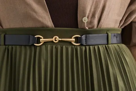 Elegancka stylizacja: oliwkowa plisowana spódnica z brązową bluzką i czarnym paskiem. Idealne połączenie, by zadać sobie pytanie: jaka bluzka do plisowanej spódnicy?