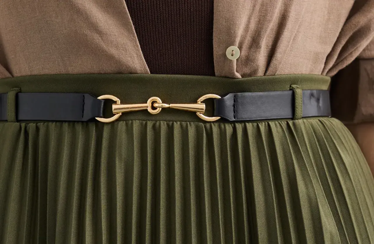 Elegancka stylizacja: oliwkowa plisowana spódnica z brązową bluzką i czarnym paskiem. Idealne połączenie, by zadać sobie pytanie: jaka bluzka do plisowanej spódnicy?