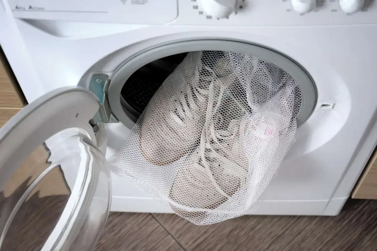 Białe buty sportowe w siatkowej torbie, gotowe do prania w pralce. Dowiedz się, jak prać buty w pralce, by odświeżyć je bez ryzyka.